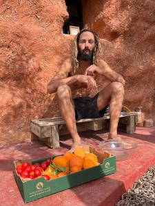 un hombre sentado en un banco junto a una caja de fruta en Le Khaïma Bio, Oasis écologique au bord de l'océan, en Douaïra