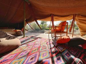 a room with a bed and a chair in a tent at Le Khaïma Bio, Oasis écologique au bord de l'océan in Douaïra