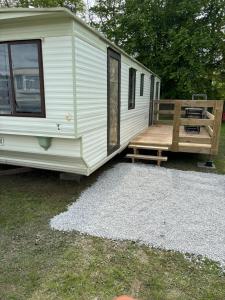 Une caravane blanche avec une véranda et une rampe en bois dans l'établissement Mobil-home camping 4 étoiles N35, à Fourmies