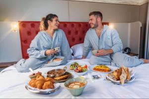 a man and a woman sitting on a bed with food at Hyatt Centric Jumeirah Dubai - Executive Room - UAE in Dubai