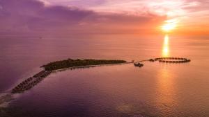 eine Insel im Ozean mit Sonnenuntergang im Hintergrund in der Unterkunft Coco Bodu Hithi in Nord-Malé-Atoll