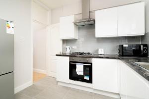 een keuken met witte kasten en een fornuis met oven bij 2 bedroom flat near Tottenham Hotspur Stadium in Londen