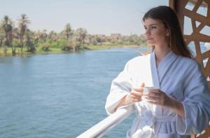una mujer parada en un puente con una taza de café en Five Star Nile Cruise from Aswan to Luxor, en Asuán