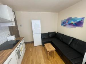 a living room with a black couch and a kitchen at 2 Bed Flat near Heathrow Airport & Elizabeth Line in Hayes
