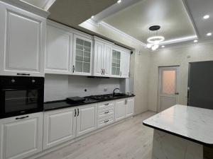 een keuken met witte kasten en zwarte apparaten bij Квартира на Мурас Ордо in Osh