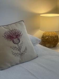 a pillow with a flower on it next to a lamp at Kinneuchar Cottage - by Elie, Dog Friendly. in Kilconquhar