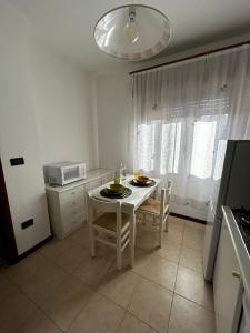 eine weiße Küche mit einem Tisch, Stühlen und einer Mikrowelle in der Unterkunft IG House - Apartment Cavallino Treporti in Cavallino-Treporti