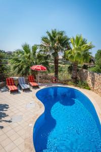 a swimming pool with two chairs and an umbrella and palm trees at 3 Bedroom Holiday Home with Private Pool and Views in Nadur