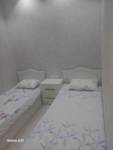 um quarto com 2 camas com lençóis brancos e uma mesa de cabeceira em Apart Khujand em Khujand