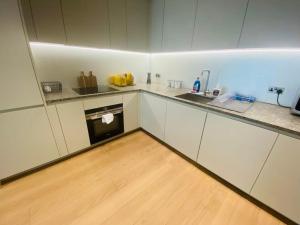 Elle comprend une petite cuisine avec des placards blancs et du parquet. dans l'établissement Lovely 2Bedroom Apartment at O2 London 01, à Londres