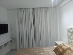 a bedroom with a bed and a tv and curtains at LEON MARIA HOSPEDAGENS - Smart Flat Hotel e Residence in Mogi das Cruzes