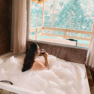 a woman in a bath tub taking a picture of a window at Sítio caminho das nascentes in Urubici