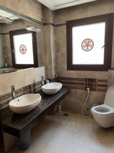 ein Badezimmer mit zwei Waschbecken, einem WC und zwei Fenstern in der Unterkunft الشيخ زايد in Sheikh Zayed