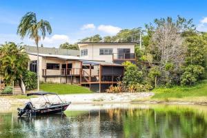 a house on the shore of a body of water with a boat at Lakefront Living in Burleigh in Gold Coast