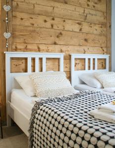 2 witte bedden in een kamer met een houten muur bij Apartamenty sudeckie nad zalewem III in Marczyce