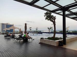 un hombre sentado en una silla junto a una piscina en Comodo Apartemen Pollux Habibie Rooftop-SeaView en Batam Center