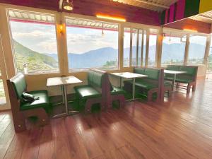 un restaurante con mesas, sillas verdes y ventanas grandes en Rolled Guest house, en Phagwāra