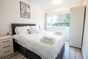 um quarto com uma cama com lençóis brancos e uma janela em Stylish 2BR Retreat - Near Station, Free Parking em Raynes Park