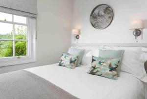 een wit bed met kussens en een spiegel aan de muur bij A beautiful Cotswolds Cottage in Stroud in Stroud