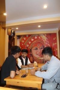 um grupo de pessoas sentadas à mesa com um quadro de uma mulher em Jhigu Chhen em Bhaktapur