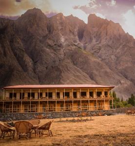 a building with tables and chairs in front of a mountain at Guzel Hotel in Shigar