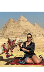 a woman sitting next to a camel in front of the pyramids at Falcon pyramids inn in Cairo