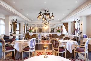 ein Restaurant mit Tischen, Stühlen und einem Kronleuchter in der Unterkunft Auberge du Jeu de Paume in Chantilly