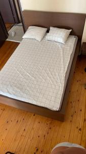 uma cama com lençóis brancos e almofadas num piso de madeira em Friendly guest house em Tessalônica