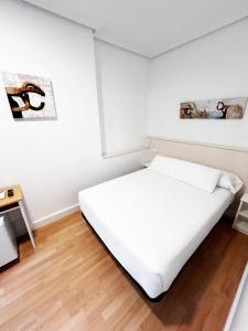 a white bedroom with a bed and a table at Pensión Régil in San Sebastián