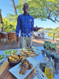 Ein Mann steht vor einem Tisch voller Essen. in der Unterkunft Zambezi Dusk in Livingstone