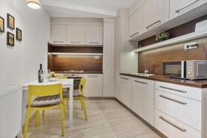 a kitchen with white cabinets and a table and yellow chairs at Apple apartment in Bratislava