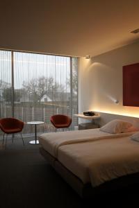 a bedroom with a bed and two chairs and a large window at D-Hotel in Kortrijk