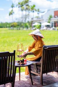 Kobieta w kapeluszu siedząca na ławce w obiekcie Chez Mimosa Rice Farm Hoi An - New address DX18, Thanh Nhut, Cam Thanh w Hoi An