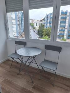 dwa krzesła i stół w pokoju z dwoma oknami w obiekcie Lisbon South Bay Rooms 2 w mieście Almada