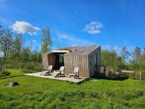 a small wooden cabin with chairs in a field at Tiny house De Wylp in Westergeest