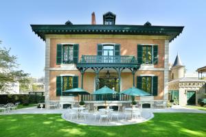 uma grande casa de tijolos com uma varanda, mesas e cadeiras em 4 chambres au Chalet Clermont-Tonnerre + piscine em Vichy