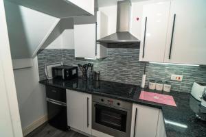a kitchen with white cabinets and a stove top oven at Beachmount Holiday Apartments in Colwyn Bay