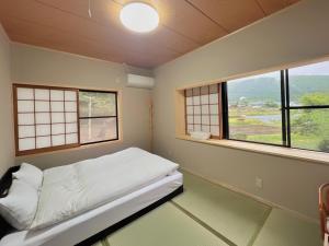 a small room with a bed and two windows at 湯布院我楽珍民泊Yufuin Garakuchin in Yufuin