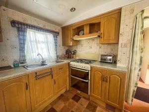 a kitchen with wooden cabinets and a sink and a stove at 6 Berth Caravan With Decking Nearby Heacham Beach In Norfolk Ref 21047a in Heacham