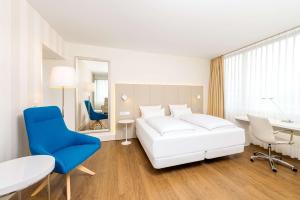 a bedroom with a white bed and a blue chair at NH Erlangen in Erlangen
