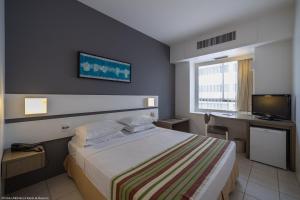 Habitación de hotel con cama, escritorio y TV. en Oasis Imperial & Fortaleza en Fortaleza