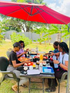 un grupo de personas sentadas en una mesa de picnic bajo un paraguas en Bruks Guest House, en Kumasi