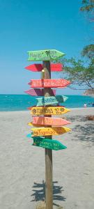 - un panneau directionnel sur la plage avec l'océan dans l'établissement Playa del Ritmo Beach Hostel & Bar - Adults Only, à Santa Marta