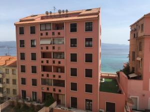ein hohes rosa Gebäude mit dem Meer im Hintergrund in der Unterkunft L'Ajax Appartement T3 centre et Bord de mer in Ajaccio