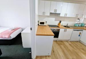 a small kitchen with white cabinets and a bed at Chic 2 Bed Apartment On Scarborough Beach in Perth