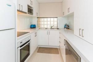 een witte keuken met witte kasten en een wastafel bij The White Pearl Penthouse in Perth