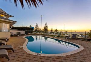 a swimming pool in a patio with chairs and the ocean at Sunset On Esplanade in Perth