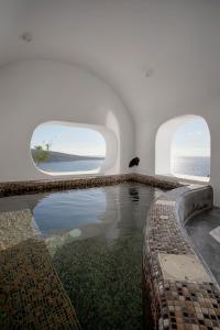 a swimming pool with two windows in a white building at ArmonOia Luxury Caves in Oia