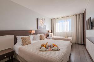 サント・マキシムにあるオテル ラ プラージュのベッド2台、ベッドの上に食料トレイが備わるホテルルームです。