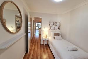 a white bedroom with a large mirror and a bed at Beach Break Iconic Scarborough in Perth